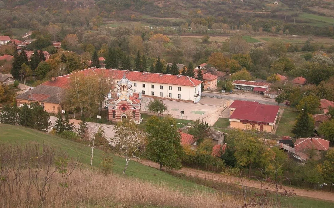 Есенна панорама на Димово отвисоко с раираната тухлена църква и керемидените покриви сред пъстрите дървета и ниските хълмове