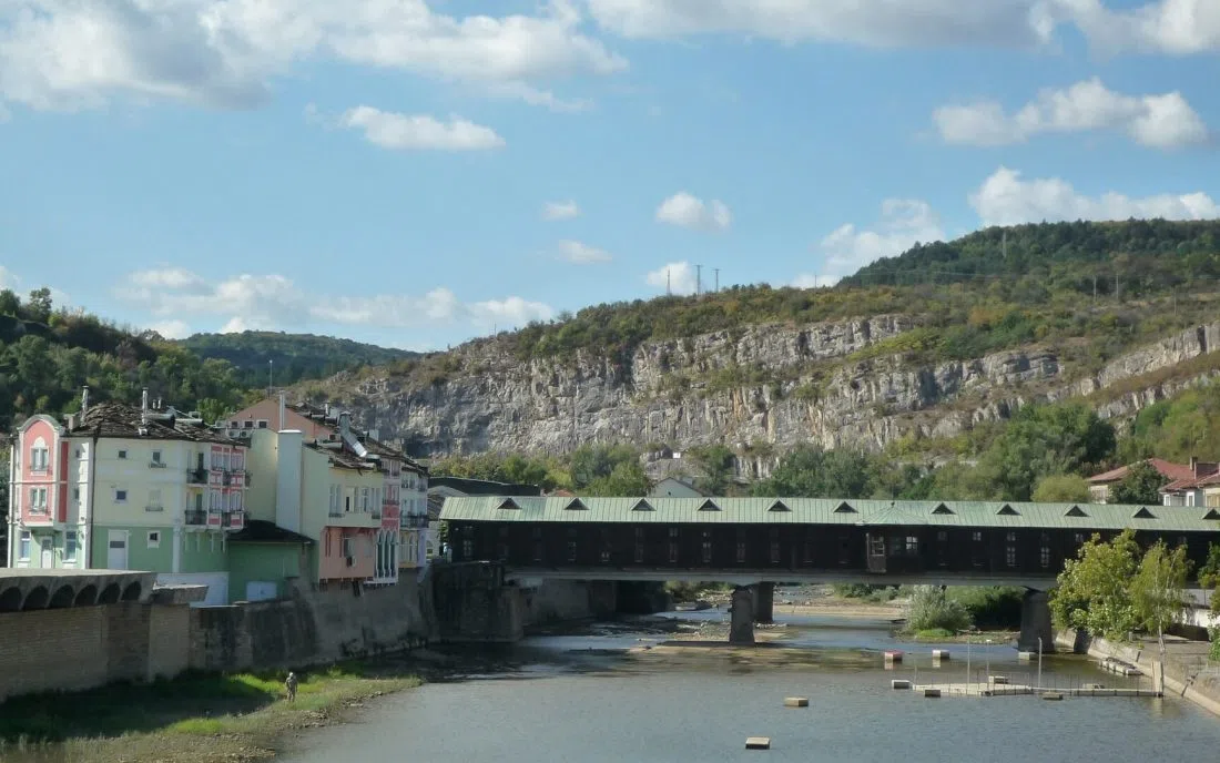 Покритият мост в Ловеч над река Осъм със зелен ламаринен покрив и скалите зад него