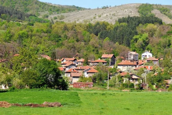 Каменни къщи с червени покриви под зелен склон в Драгодан