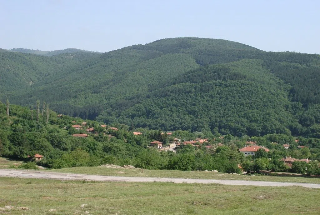 Планинско село с керемидени покриви, потънало в зеленина в подножието на гористи била на източна Стара планина