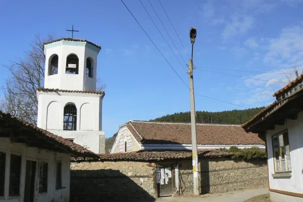 Белосаната камбанария на селската църква над каменния зид в Поибрене