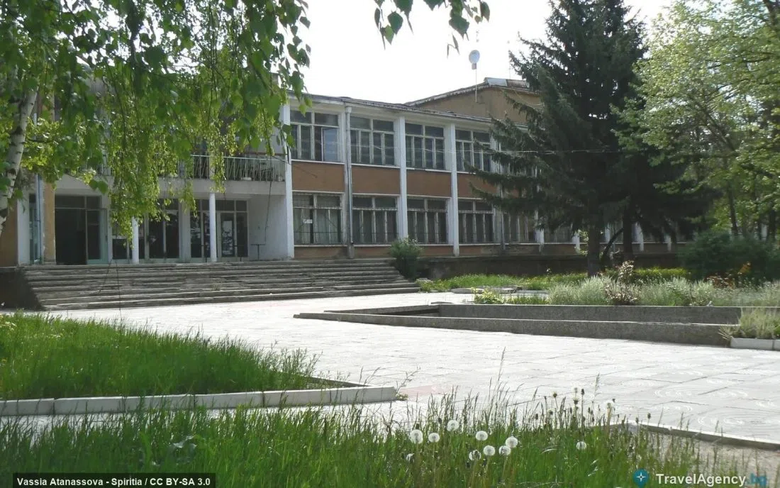Обществена сграда с колонада и широки стъпала сред зеленина в Батановци