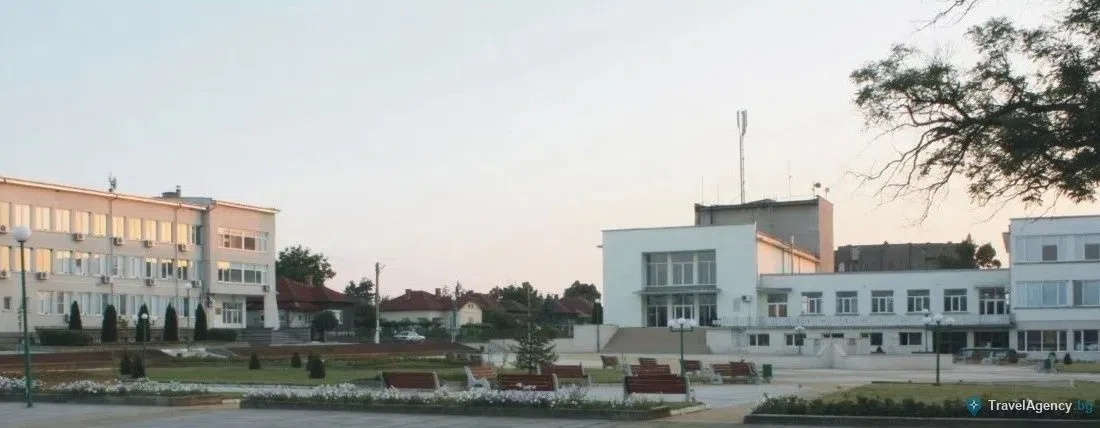 Площадът в центъра на Брусарци с цветни лехи, пейки и обществени сгради