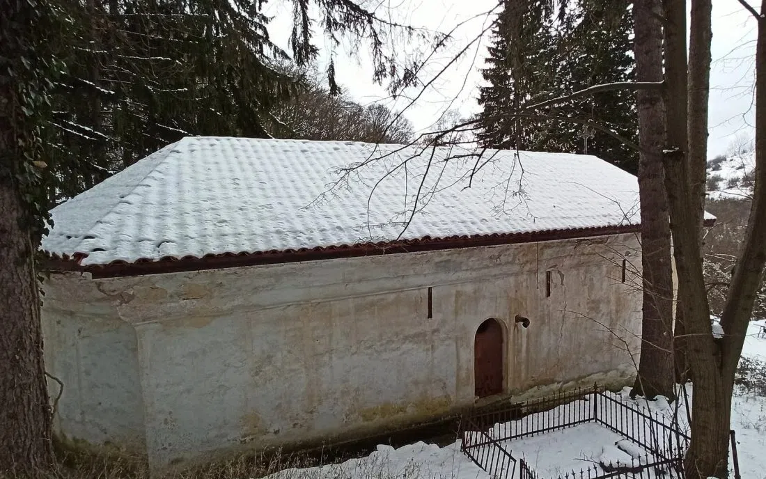 Стара манастирска църква с бял хоросан и заснежен покрив сред зимна гора