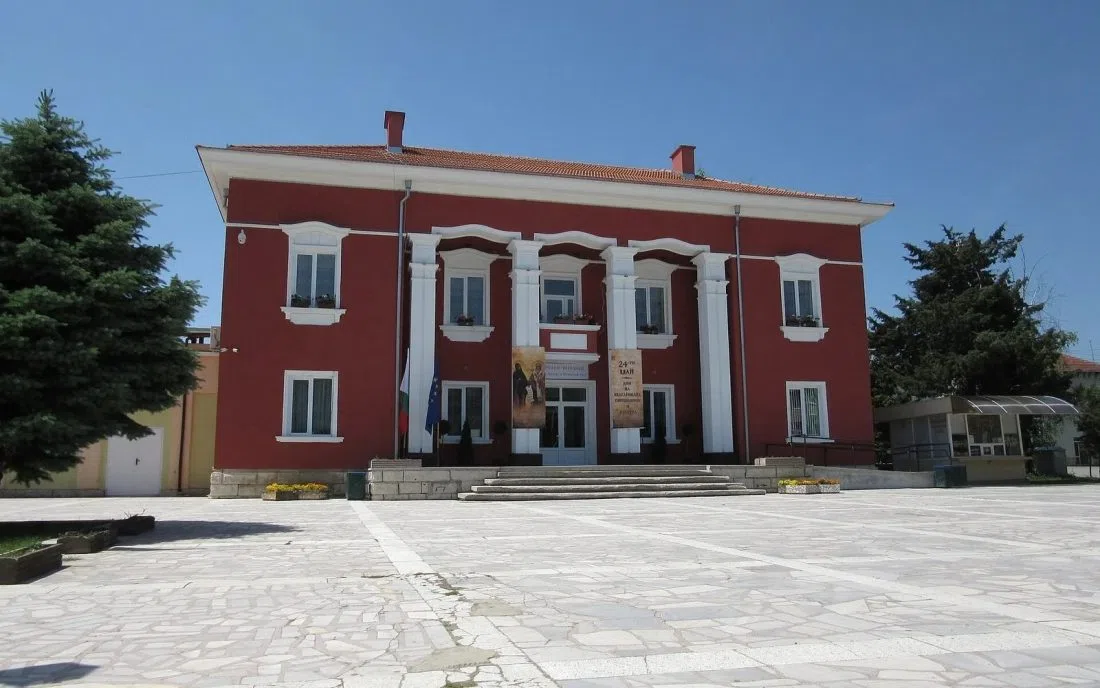 Червената сграда на читалището с бели колони на площада в Две могили